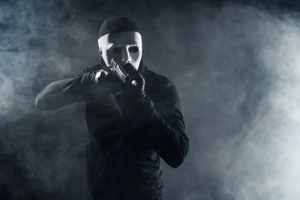 Uomo in maschera e passamontagna puntando con pistola e torcia — Foto stock