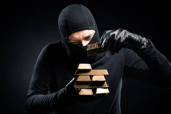 Robber in balaclava stacking gold bullions in his hands — Stock Photo