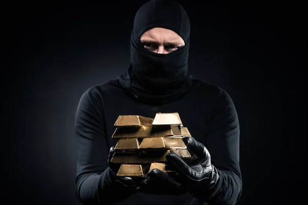 Hombre en pasamontañas sosteniendo lingotes de oro en sus manos - foto de stock