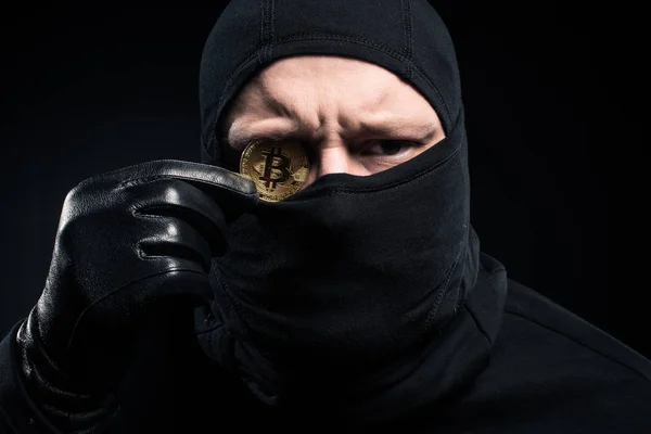 Criminal em balaclava preta segurando bitcoin dourado — Fotografia de Stock