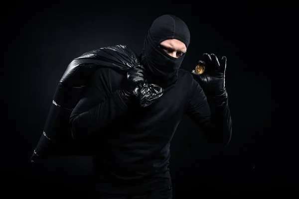 Homem em balaclava segurando saco de plástico com dinheiro e bitcoin — Fotografia de Stock