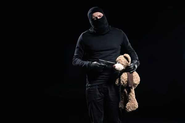 Burglar in balaclava holding gun and teddy bear — Stock Photo