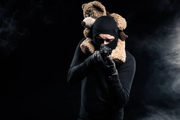 Homme avec un ours en peluche sur le cou visant avec une arme — Photo de stock