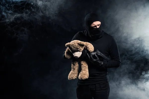 Kidnapper in balaclava holding gun and teddy bear — Stock Photo