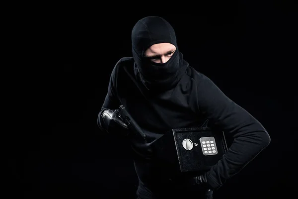 Burglar in balaclava holding gun and locked safe — Stock Photo