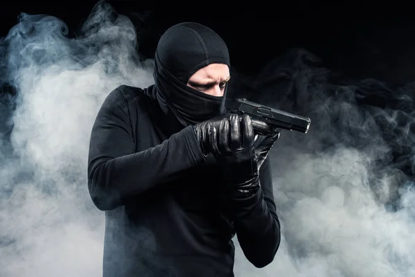 Rapinatore in passamontagna e guanti puntando con la pistola in nuvole di fumo — Foto stock