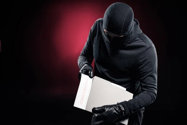 Burglar in balaclava holding confidential documents — Stock Photo