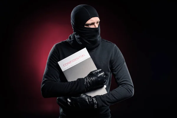 Criminal in balaclava holding confidential documents — Stock Photo