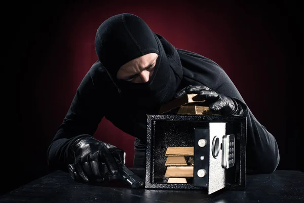 Hombre en pasamontañas con pistola robando lingotes de oro de caja fuerte - foto de stock