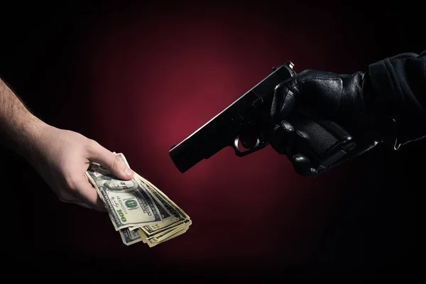Burglar with gun robbing man with dollars — Stock Photo