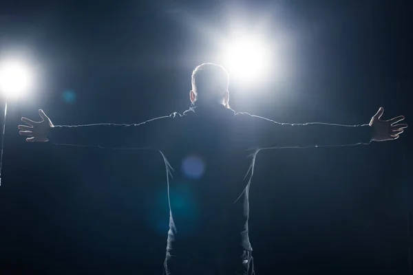 Man in black clothes standing with outstretched arms in bright light — Stock Photo