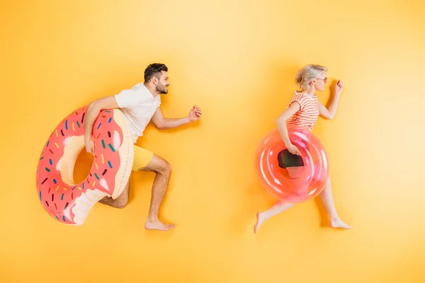 Happy young couple holding inflatable swimming rings on yellow — Stock Photo