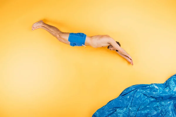 Handsome young man in shorts diving in imagine sea on yellow — Stock Photo