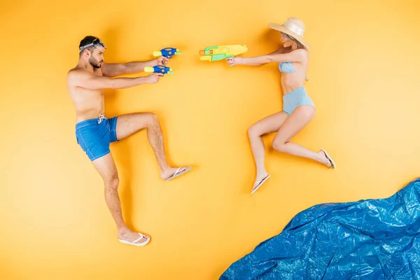 Jeune couple en maillot de bain jouant avec des pistolets à eau sur jaune — Photo de stock
