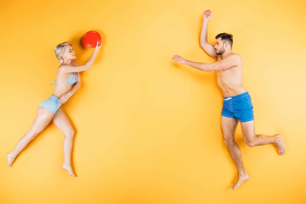 Молода пара босоніж у купальнику грає з літаючим диском на жовтому, концепція літніх канікул — стокове фото