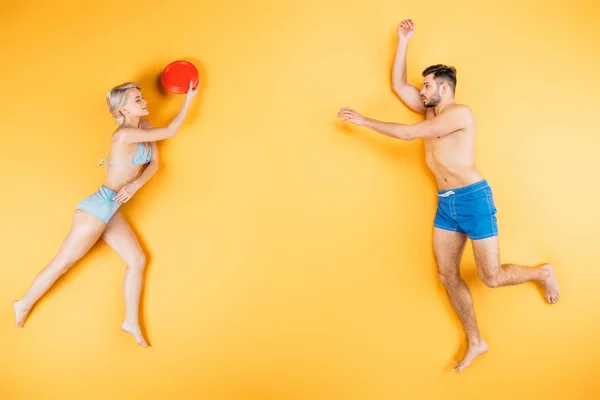 Junges Barfußpaar in Badebekleidung spielt mit fliegender Scheibe auf gelbem Sommerferienkonzept — Stockfoto