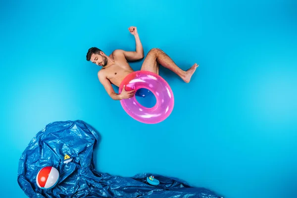 Young man holding swimming ring and looking at imagine sea with beach ball and toy ships on blue — Stock Photo