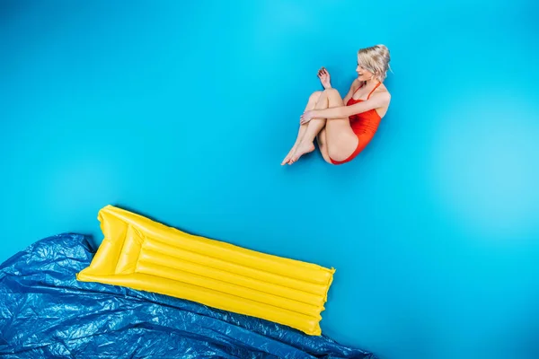 Schöne junge Frau im Badeanzug springt auf aufblasbare Matratze auf blau — Stockfoto