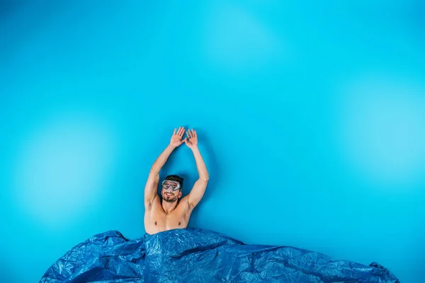 Happy young man in swimming mask raising hands from imagine waves on blue — Stock Photo