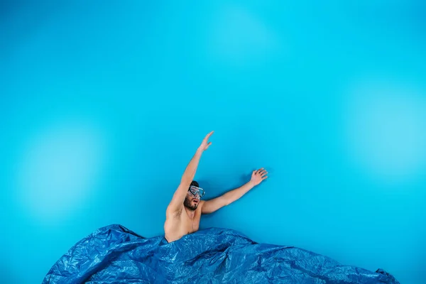 Young man in swimming mask raising hands from imagine waves on blue — Stock Photo