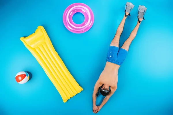 Top view of young man diving with flippers and beach items on blue — Stock Photo