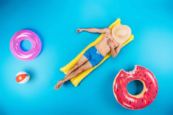 Вид зверху на молодого чоловіка в шортах, що відпочивають на надувному матраці на синьому, концепції літніх канікул — стокове фото