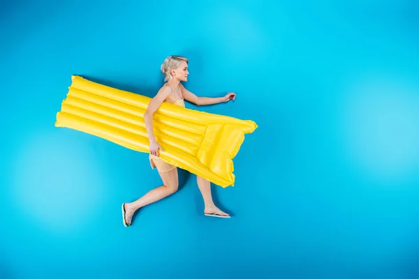 Top view of beautiful girl in flip flops holding inflatable mattress on blue — Stock Photo