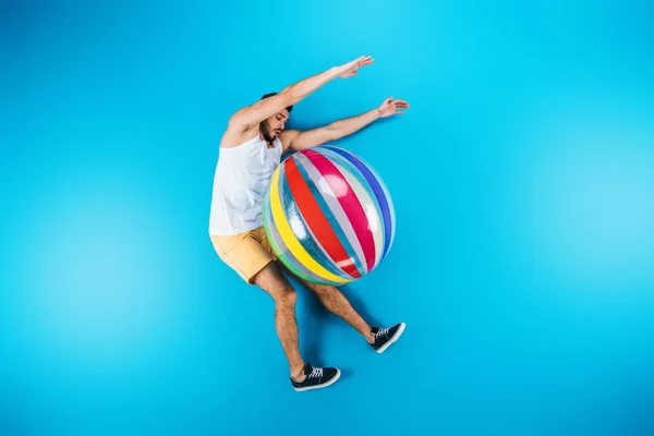 Schöner junger Mann ruht sich mit Strandball auf blauem Sommerferienkonzept aus — Stockfoto