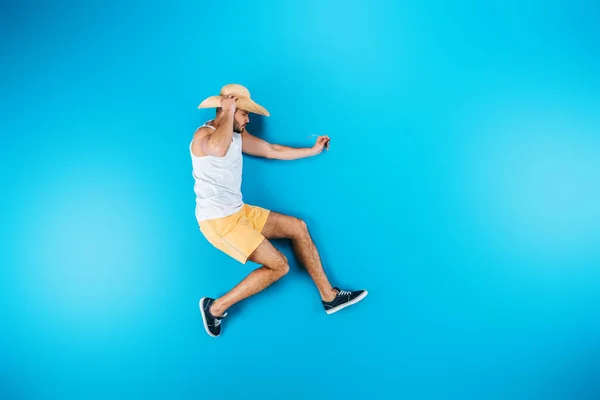 Vue de dessus du jeune homme en short et chapeau posant sur bleu — Photo de stock