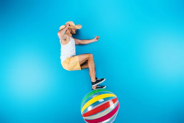 Vue de dessus du jeune homme en short et chapeau debout sur le ballon de plage sur bleu — Photo de stock