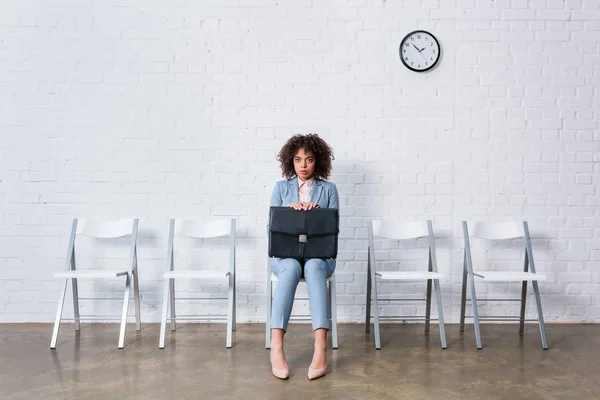 Mujer de negocios tensa con maletín sentado en la silla y esperando - foto de stock