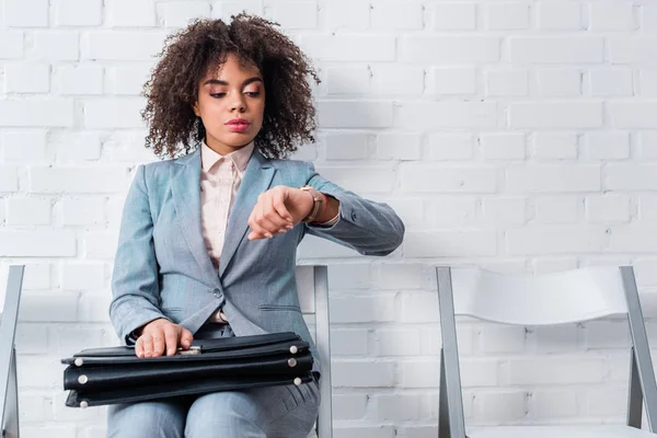 Geschäftsfrau im Anzug hält Aktentasche in der Hand und überprüft Uhr — Stockfoto