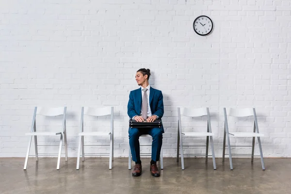 Curioso hombre con maletín esperando la entrevista mientras está sentado en la silla - foto de stock