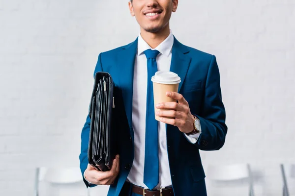 Hombre de negocios sonriente sosteniendo maletín y taza de café - foto de stock