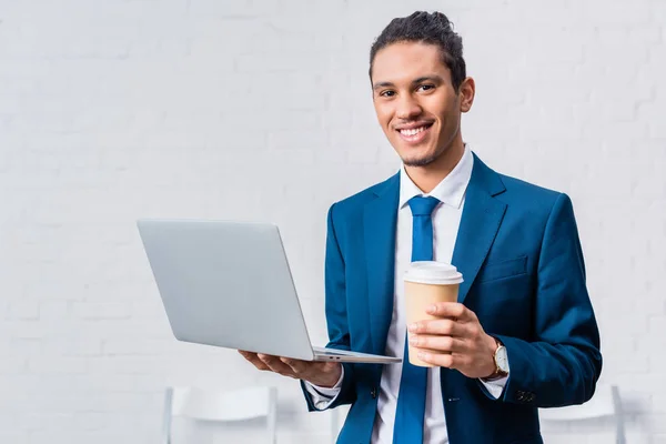 Homme d'affaires souriant tenant ordinateur portable et tasse de café — Photo de stock