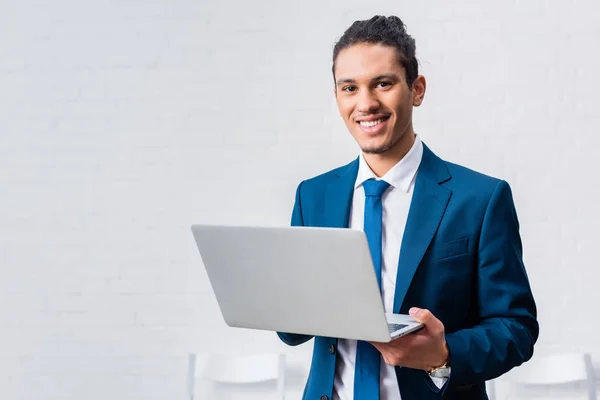 Sonriente hombre de negocios sosteniendo portátil en fondo blanco de la pared - foto de stock