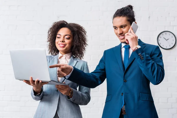 Empresario hablando por teléfono y mujer de negocios mirando el portátil - foto de stock