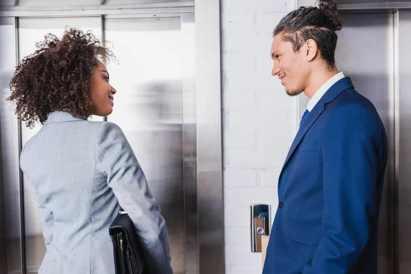 Sonriente hombre de negocios afroamericano y mujer de negocios hablando por ascensor - foto de stock