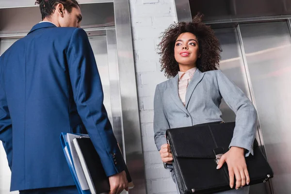 African american businesswoman with briefcase and man with folders waiting by elevator — Stock Photo