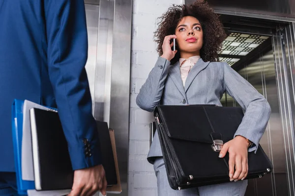 Femme d'affaires avec mallette parlant au téléphone à côté de l'homme par ascenseur — Photo de stock