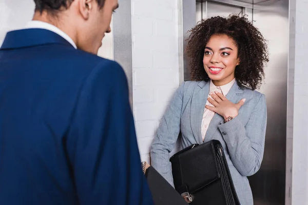 African american businesswoman with briefcase talking to man by elevator — Stock Photo