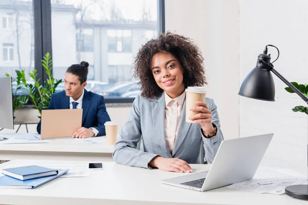 Businesswoman drinking coffee with businessman working on laptop in background — Stock Photo