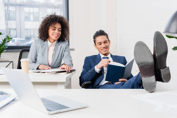 Mujer de negocios mirando al hombre sosteniendo un cuaderno en la oficina - foto de stock