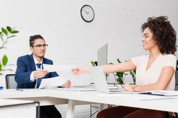 Femme d'affaires passer des papiers à l'homme d'affaires par table de travail — Photo de stock