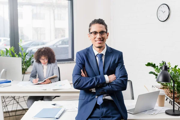 Hombre de negocios sonriente parado en el cargo con su compañera de trabajo por la mesa con la computadora - foto de stock