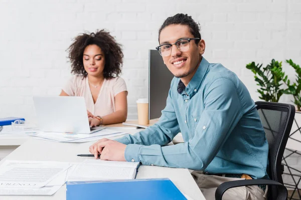 Homme d'affaires souriant travaillant dans le bureau avec une collègue féminine par table avec ordinateur portable — Photo de stock