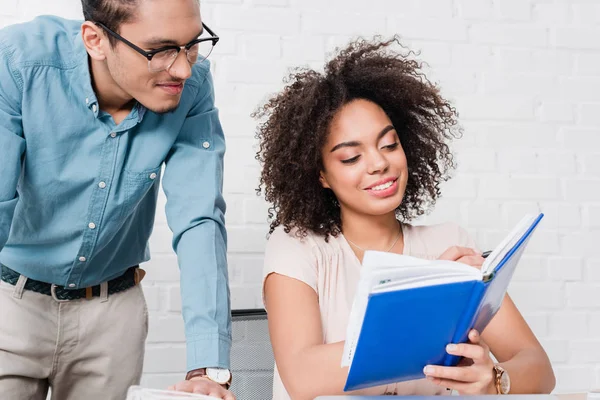 Businessman looking at woman writing in notebook in office — Stock Photo