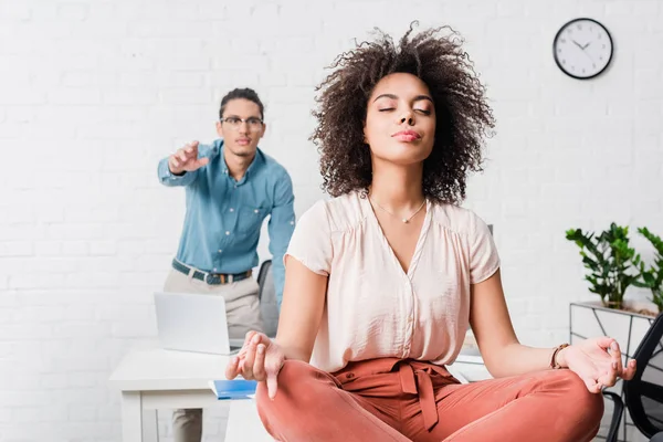 Молодая деловая женщина расслабляется и медитирует в офисе с коллегой-мужчиной позади — стоковое фото