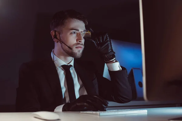 Portrait of spy agent with headset looking at computer screen at table in dark — Stock Photo