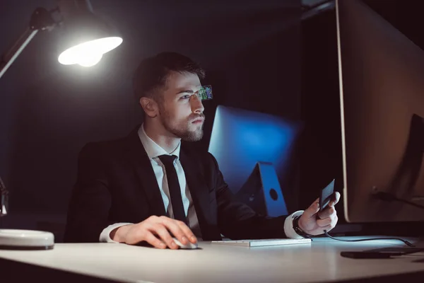 Retrato de hacker olhando para a tela do computador à mesa no escuro — Fotografia de Stock
